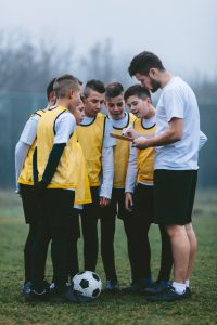 Children playing soccer. They are having training with their coach on foggy, cold, winter morning. Group is standing and coach giving them instructions for new strategy. Trainer is sketching on paper new strategy. They are dedicated to become a new soccer stars.